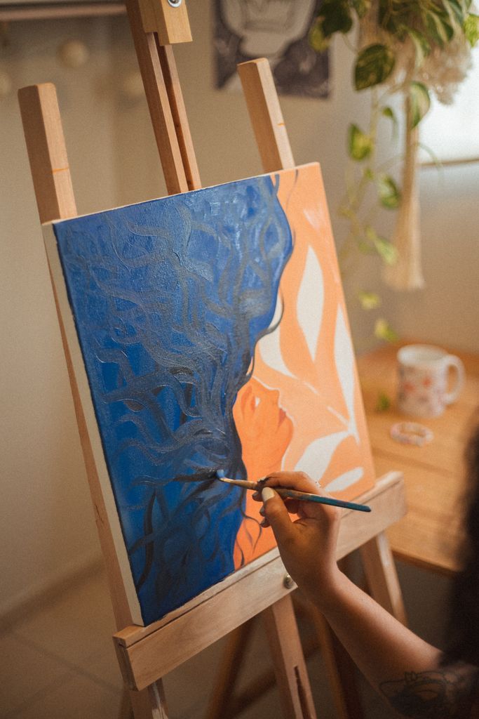 An artist skillfully paints a colorful abstract piece on an easel in a well-lit room.